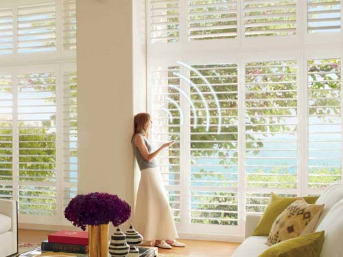 Palmbeach Polysatin Motorized Shutters - Transitional Living Room - Woman using phone to control shutters - Hunter Douglas Orange County OC