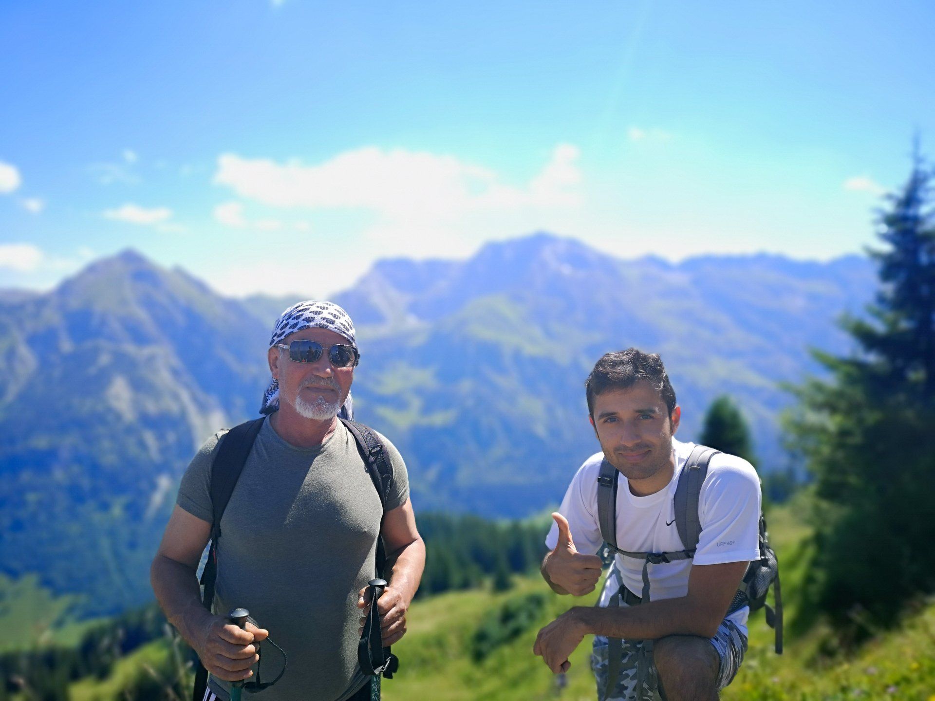 Zwei Menschen lächeln in die Kamera. Hinter ihnen ist ein gigantisches Bergpanorama zu sehen.