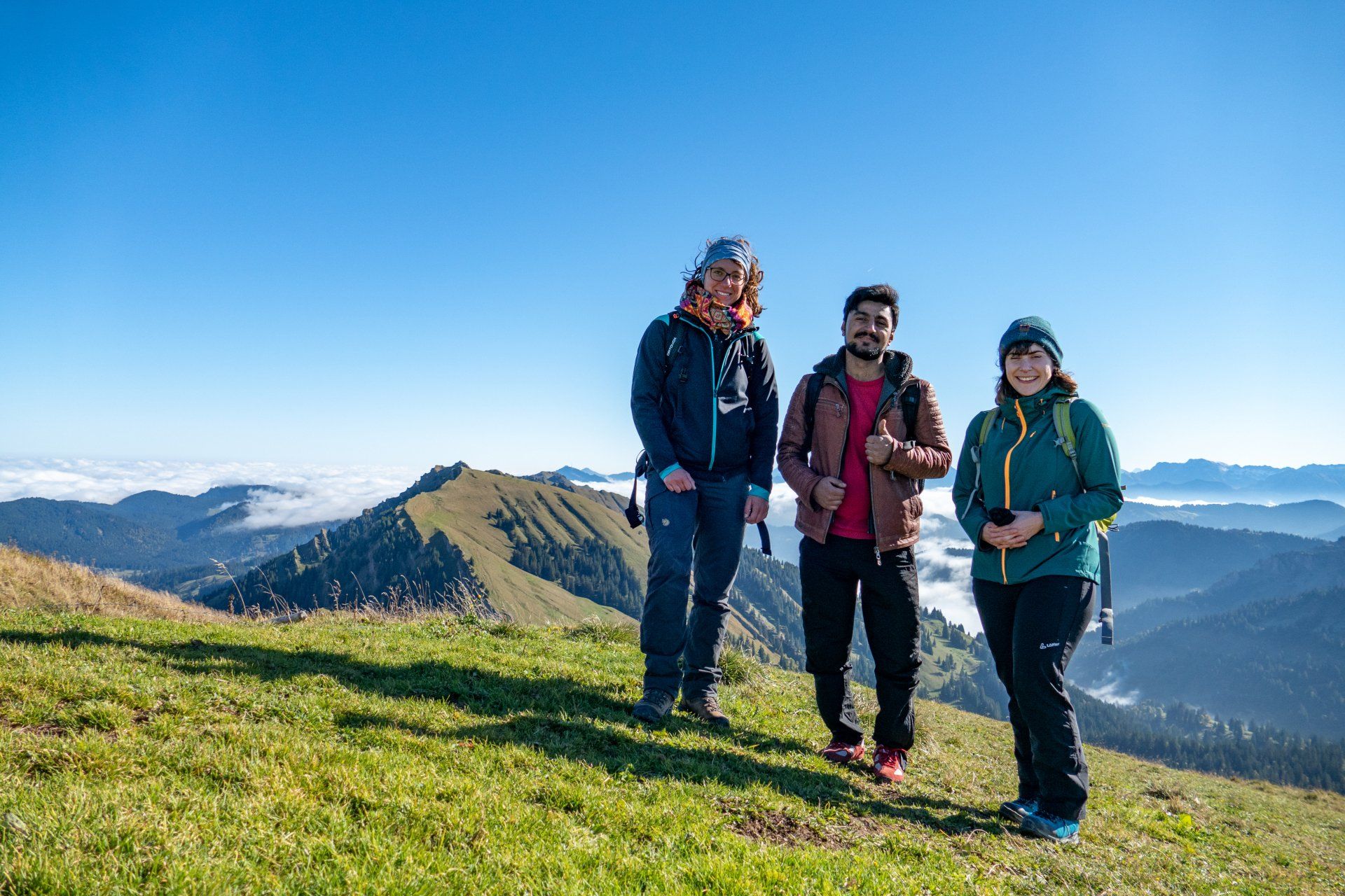 Drei Personen stehen lachend vor Bergpanorama.