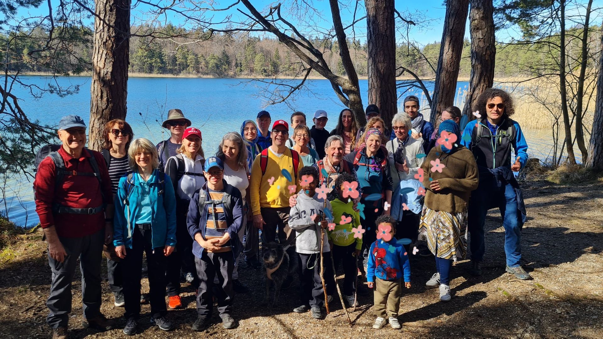 Gruppe von Erwachsenen und Kindern mit Wanderkleidung steht im Wald vor einem See an einem sonnigen Tag