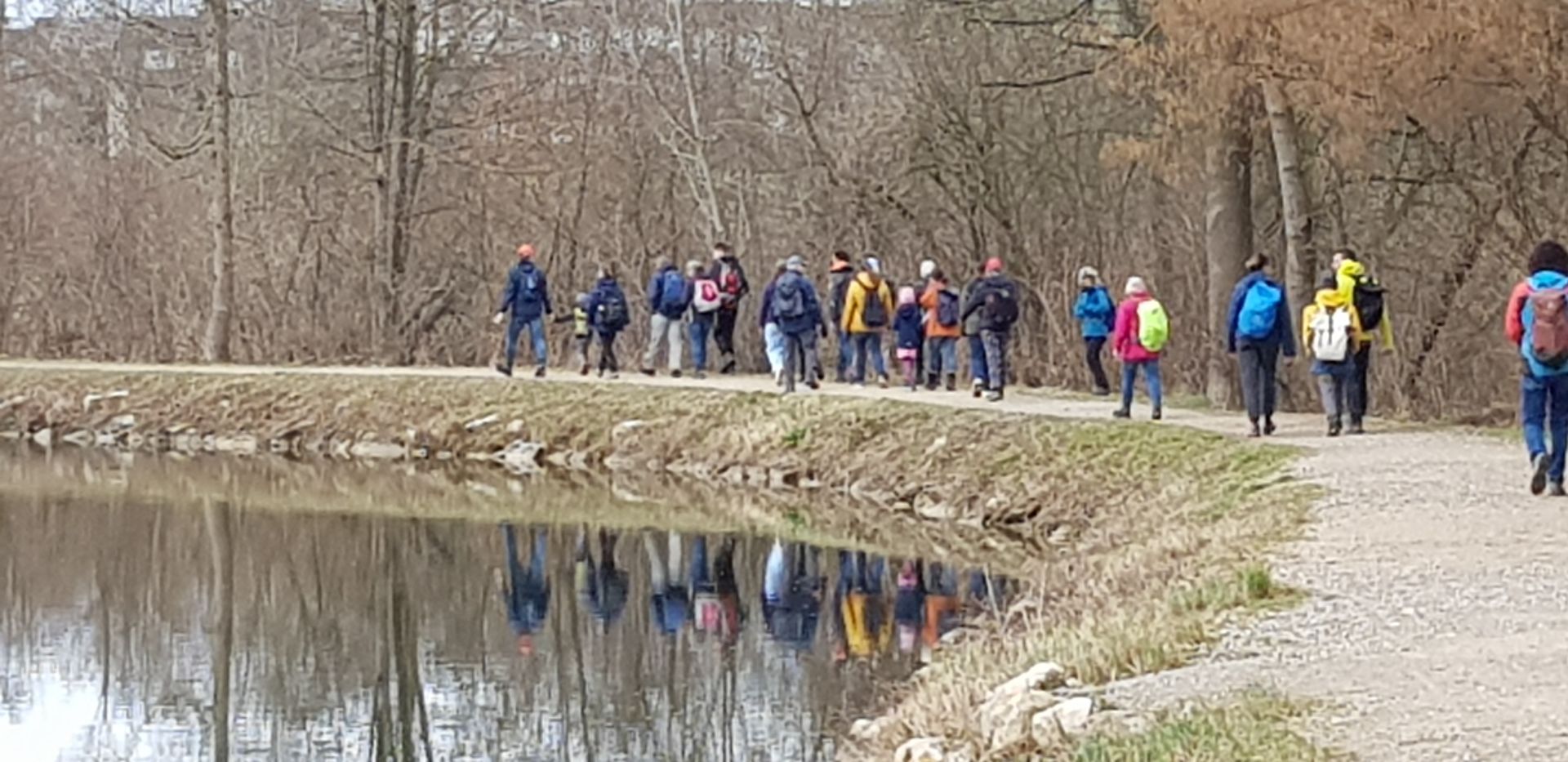 Gruppe von Menschen wandert auf einem Weg entlang eines ruhigen Sees im Wald im frühen Frühling