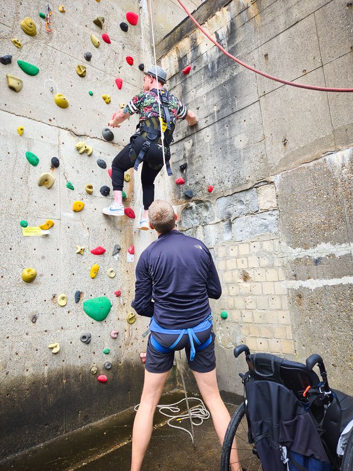 Es ist die Außenkletteranlage zu sehen. Es ist außerdem ein Sicherer und ein Kletterer zu sehen.