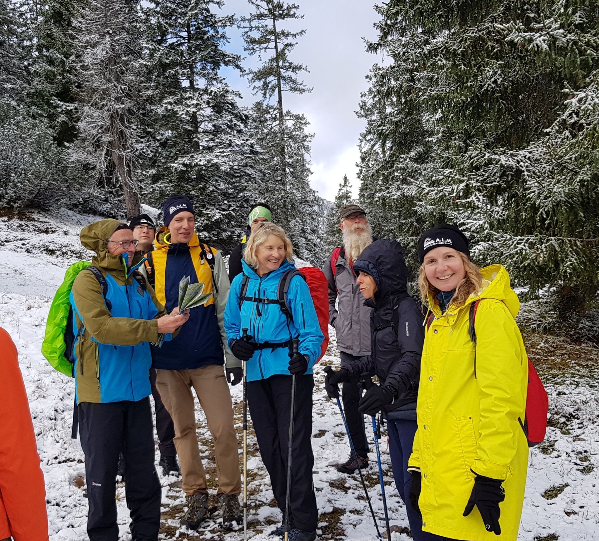 Gruppe von Wanderern in Winterkleidung mit Rucksäcken und Wanderstöcken im verschneiten Wald.