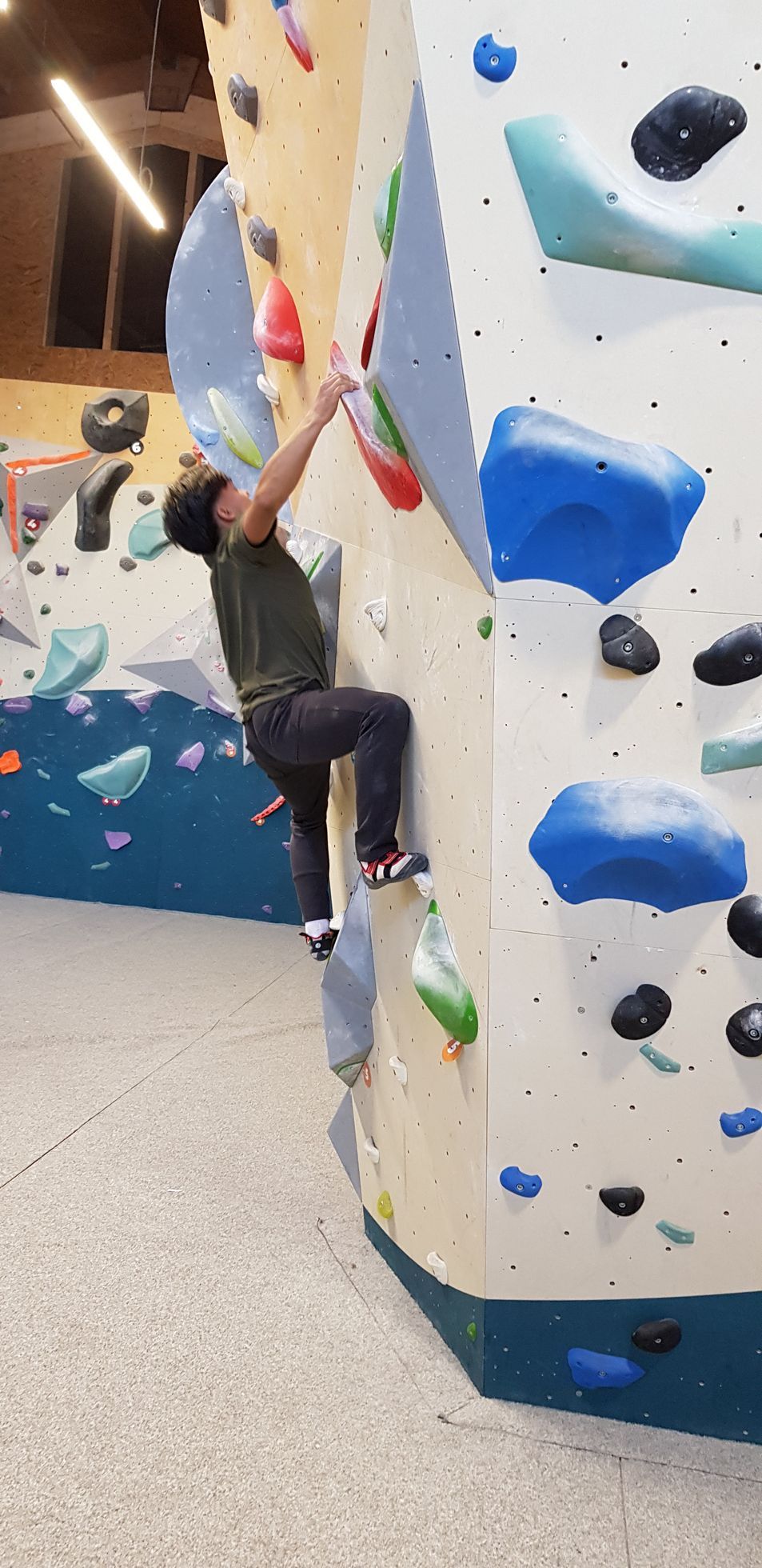 Mann klettert an einer Kletterwand mit bunten Griffen in einer Halle