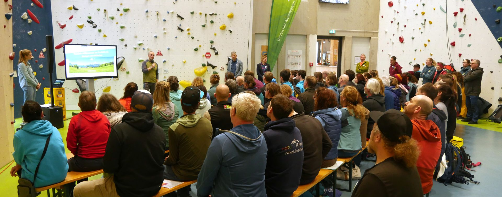 Der Horizont ist abgebildet. Im Vordergrund des Bildes ist eine Gruppe von Menschen zu sehen. Im Hintergrund sieht man eine Berg-Kette.