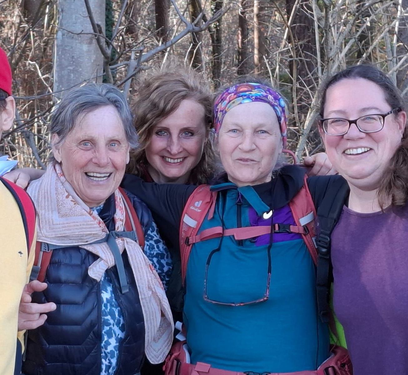 Viel Personen in Outdoor-Kleidung stehen eng zusammen vor einem Wald mit kahlen Bäumen