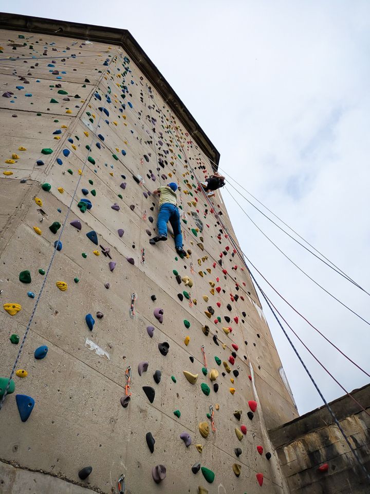 Es ist die Außenkletteranlage zu sehen. Daran klettert eine Person. Die andere wird gerade abgelassen.