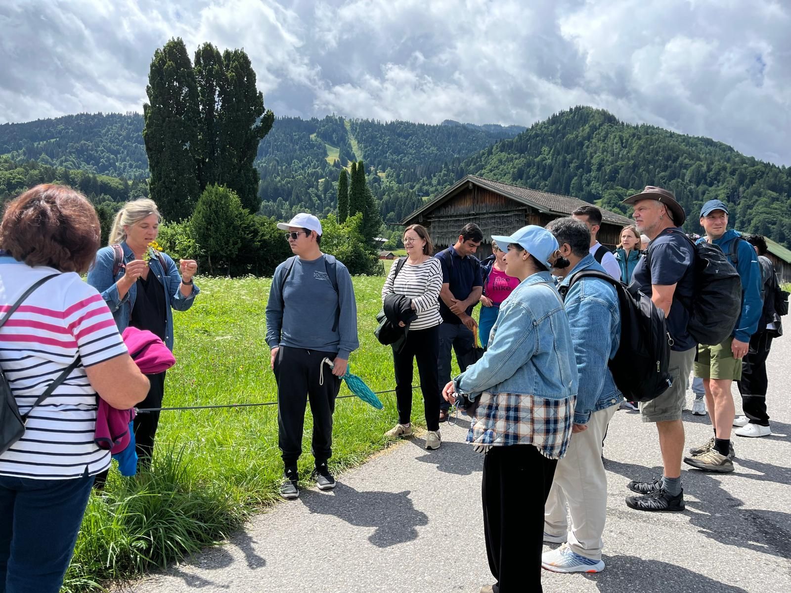Gruppe von Menschen bei einer geführten Wanderung auf einem Weg mit grünen Wiesen und bewaldeten Bergen im Hintergrund