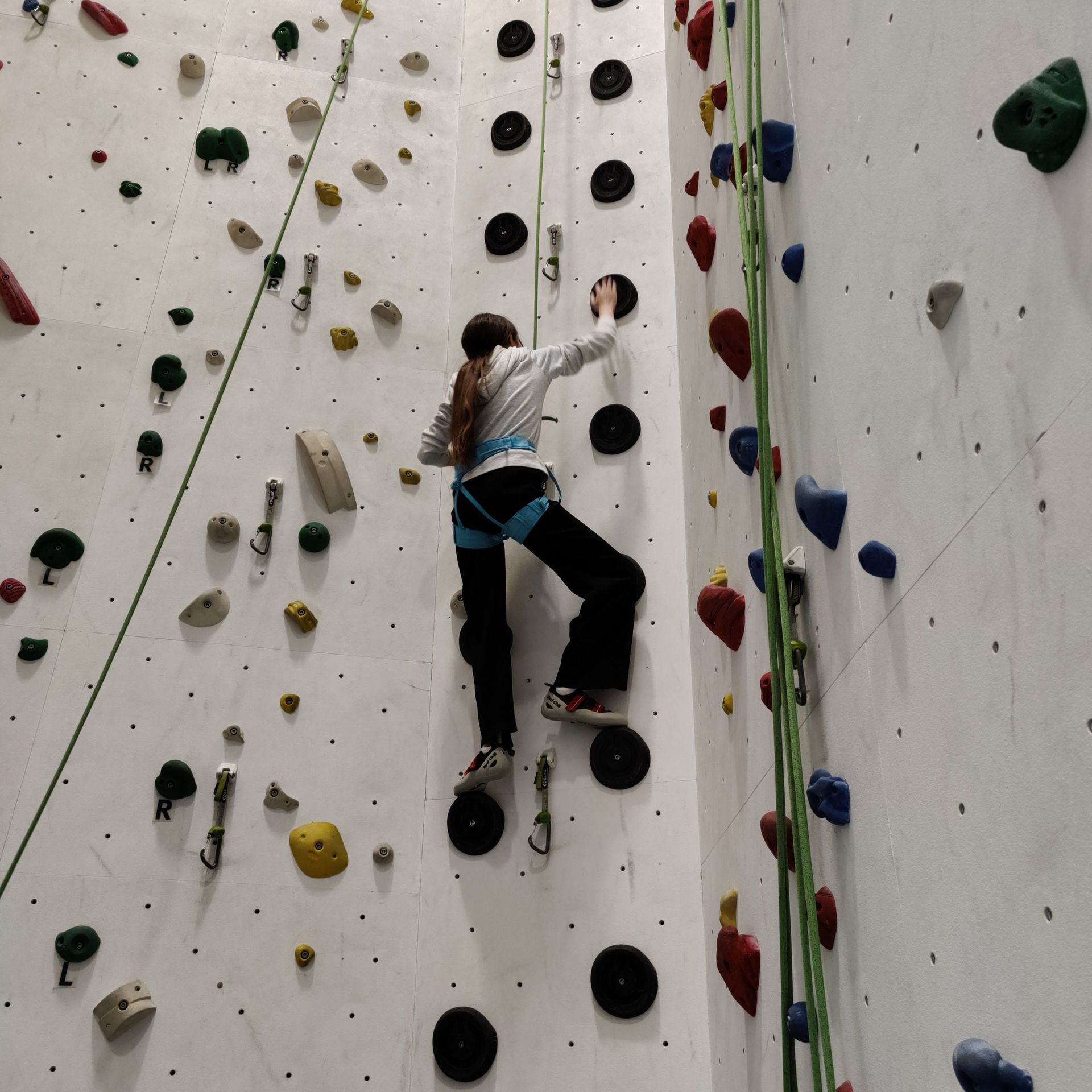 Kind mit langem Haar klettert an einer Kletterwand mit bunten Griffen in einer Halle