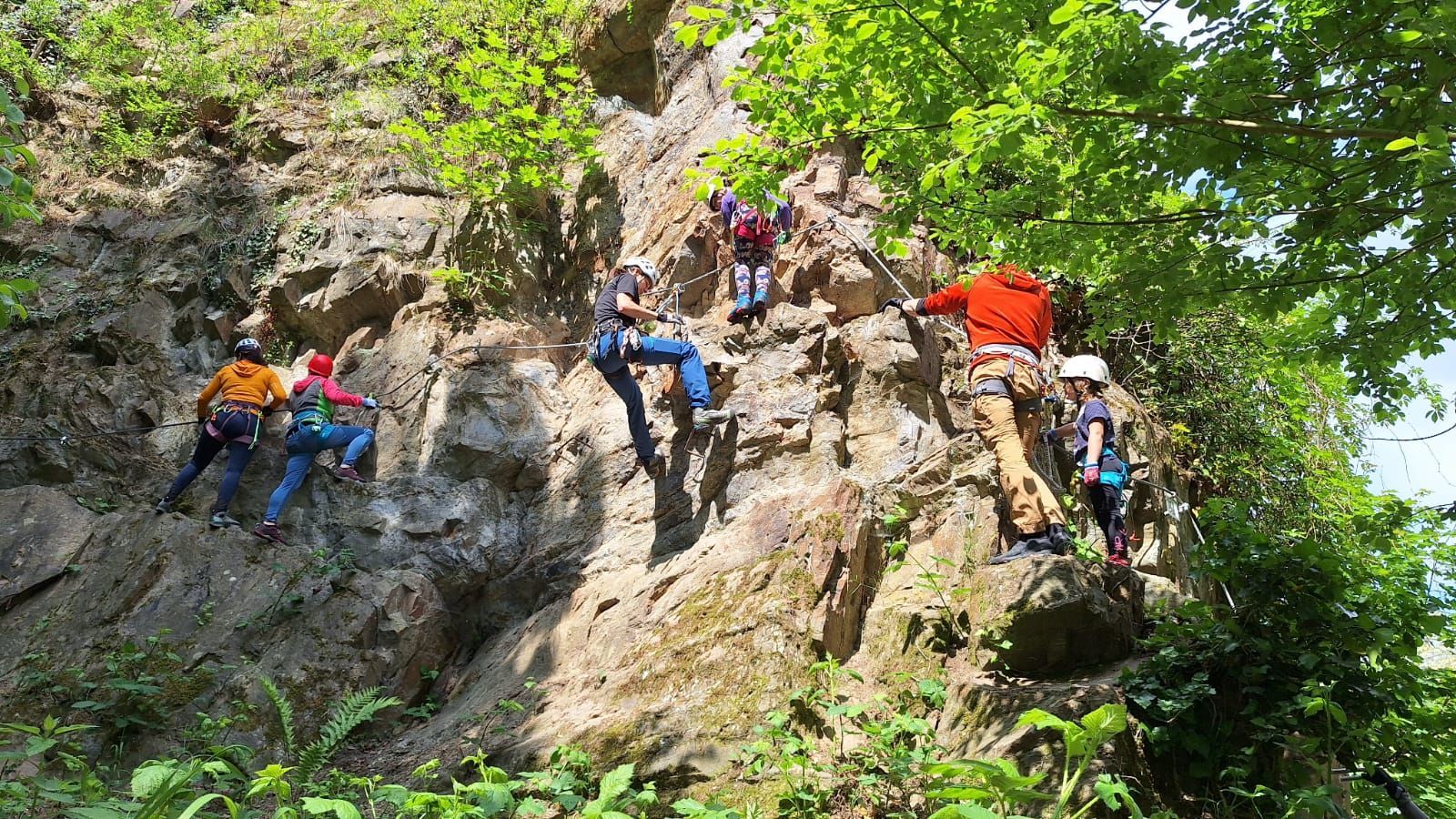 Mehrere Menschen Klettern an einem Fels an einem Klettersteig.