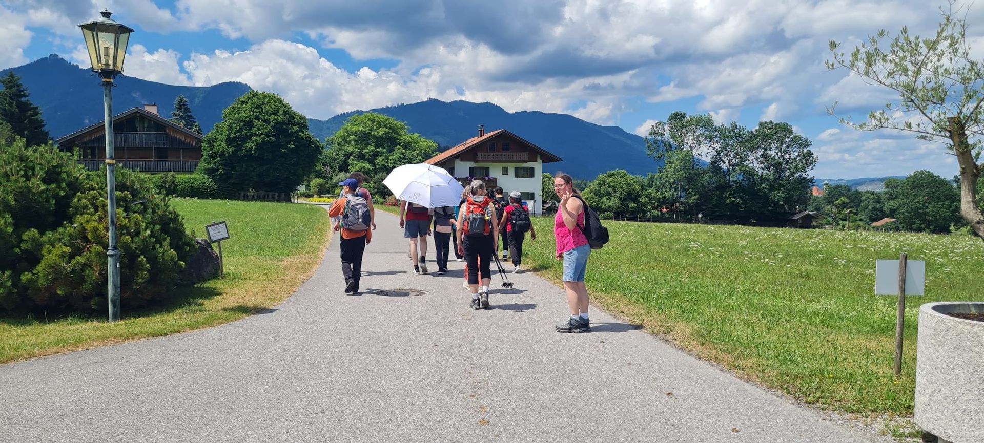 Gruppe von Wanderern, umgeben von Wiesen und Bergen im Hintergrund