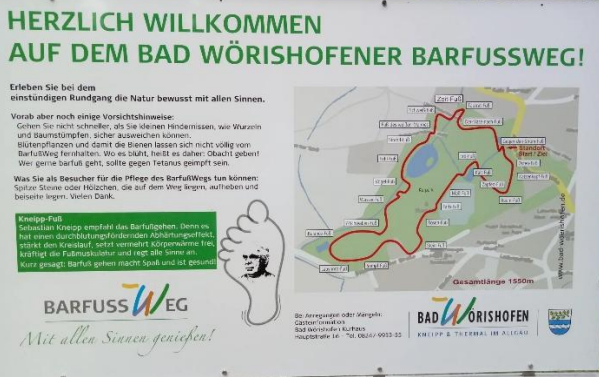 Infotafel mit grüner Überschrift 'Herzlich willkommen auf dem Bad Wörishofener Barfußweg', Text zu Vorsichtsmaßnahmen bei der Benutzung des Wegs und Pflegehinweisen für den Weg. Es gibt eine Karte des Barfußwegs mit eingezeichneten Stationen, Logos von Bad Wörishofen und Kneipp.
