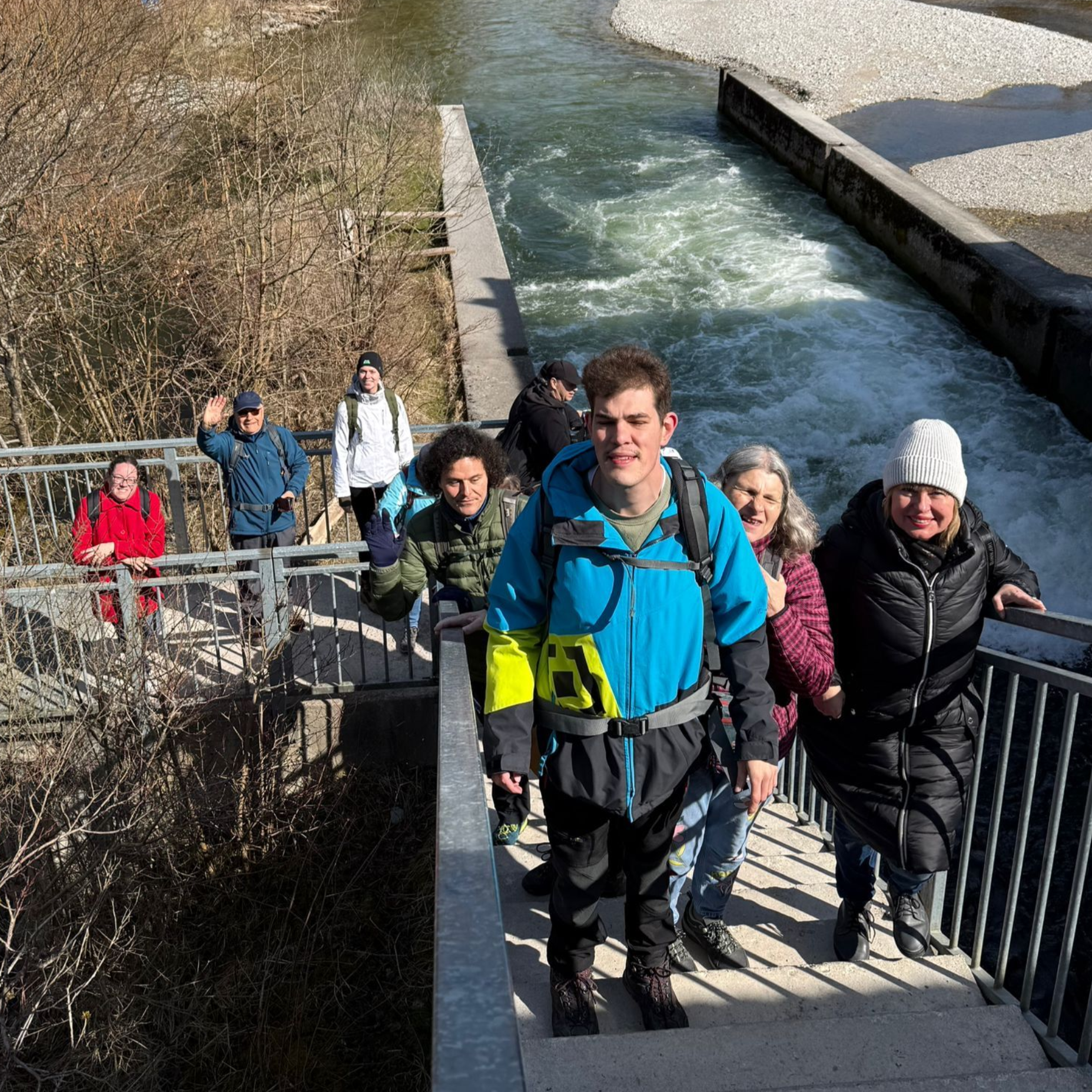 Gruppe von Wanderern steigt eine Treppe neben einem Fluss mit Kiesufer in einer bewaldeten Landschaft hinauf