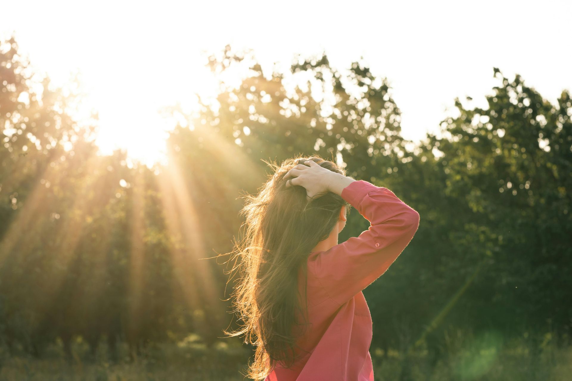 woman in nature with sun setting over trees