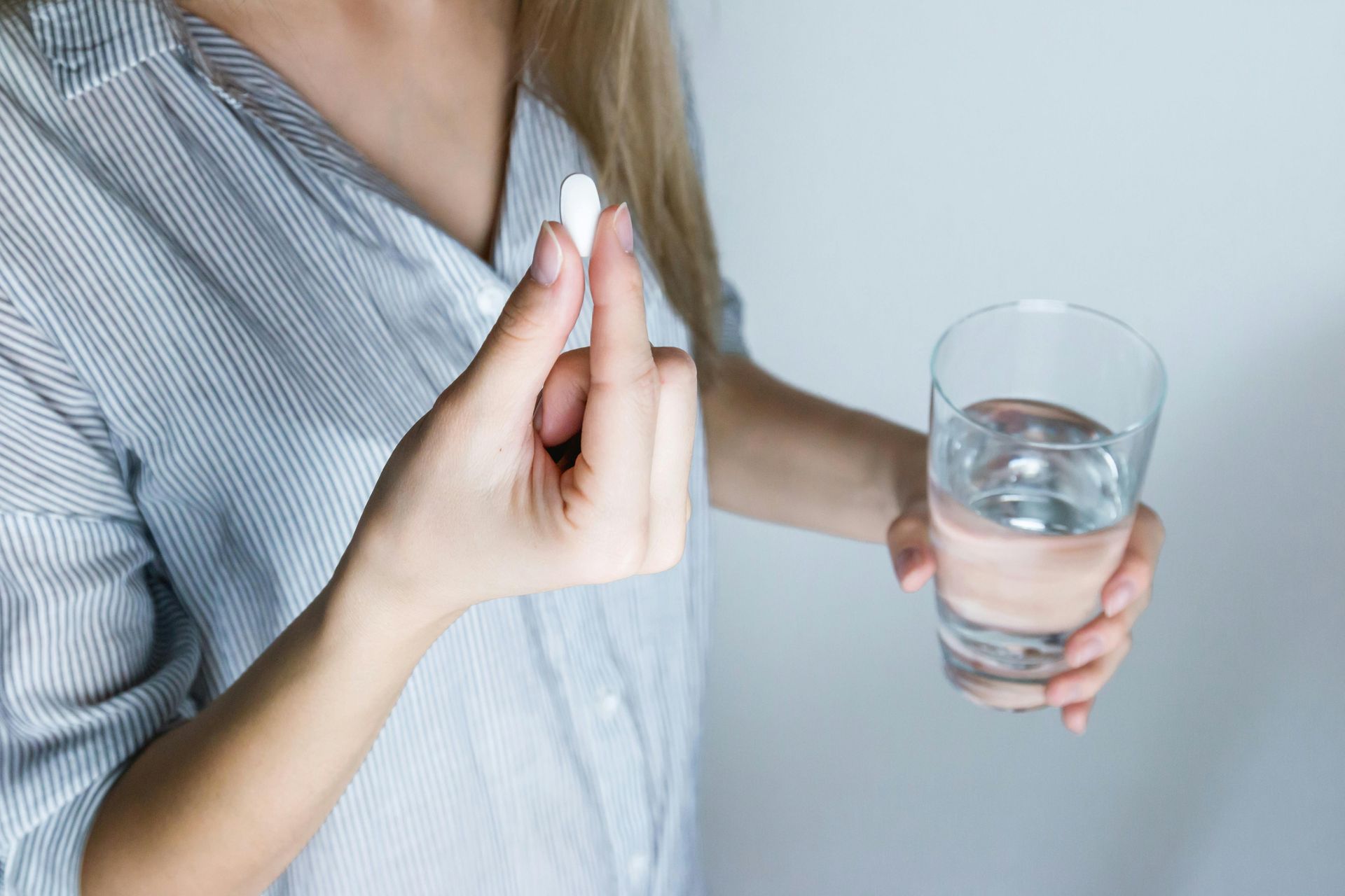 woman holding a pill and a glass of water