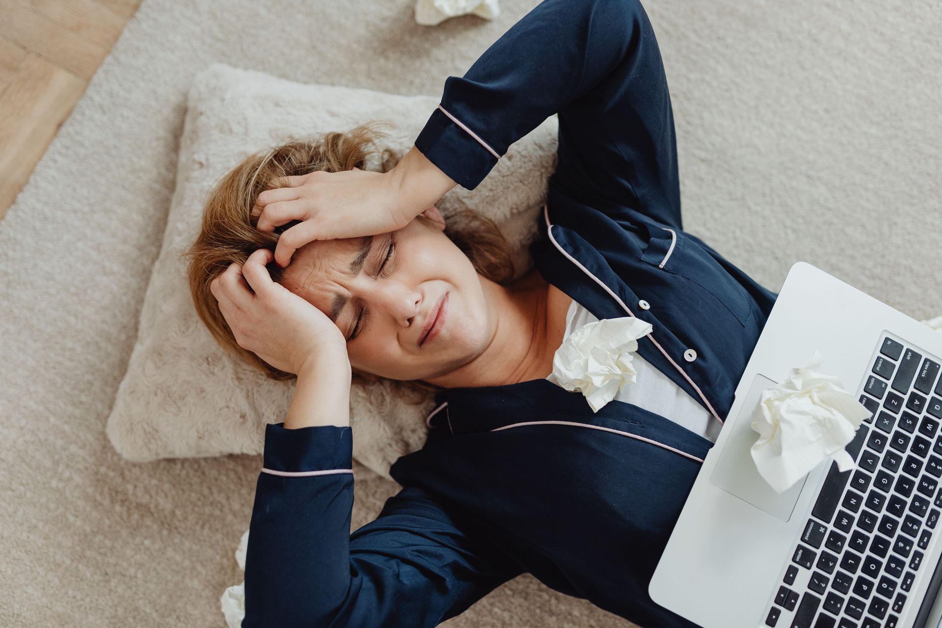 woman lying down with laptop on body and her hands on her head looking worried
