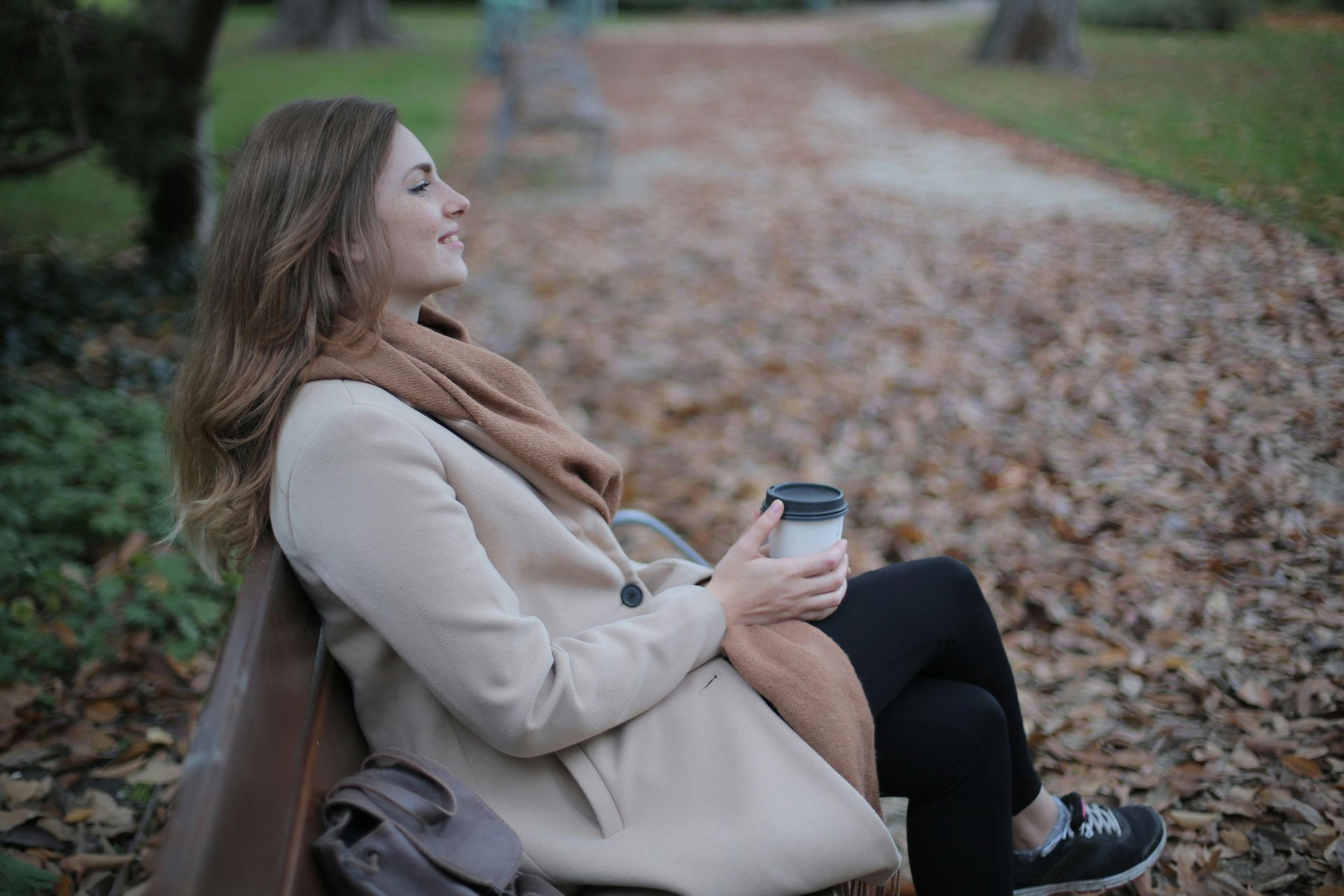 women sitting on bench in a park with a takeaway coffee
