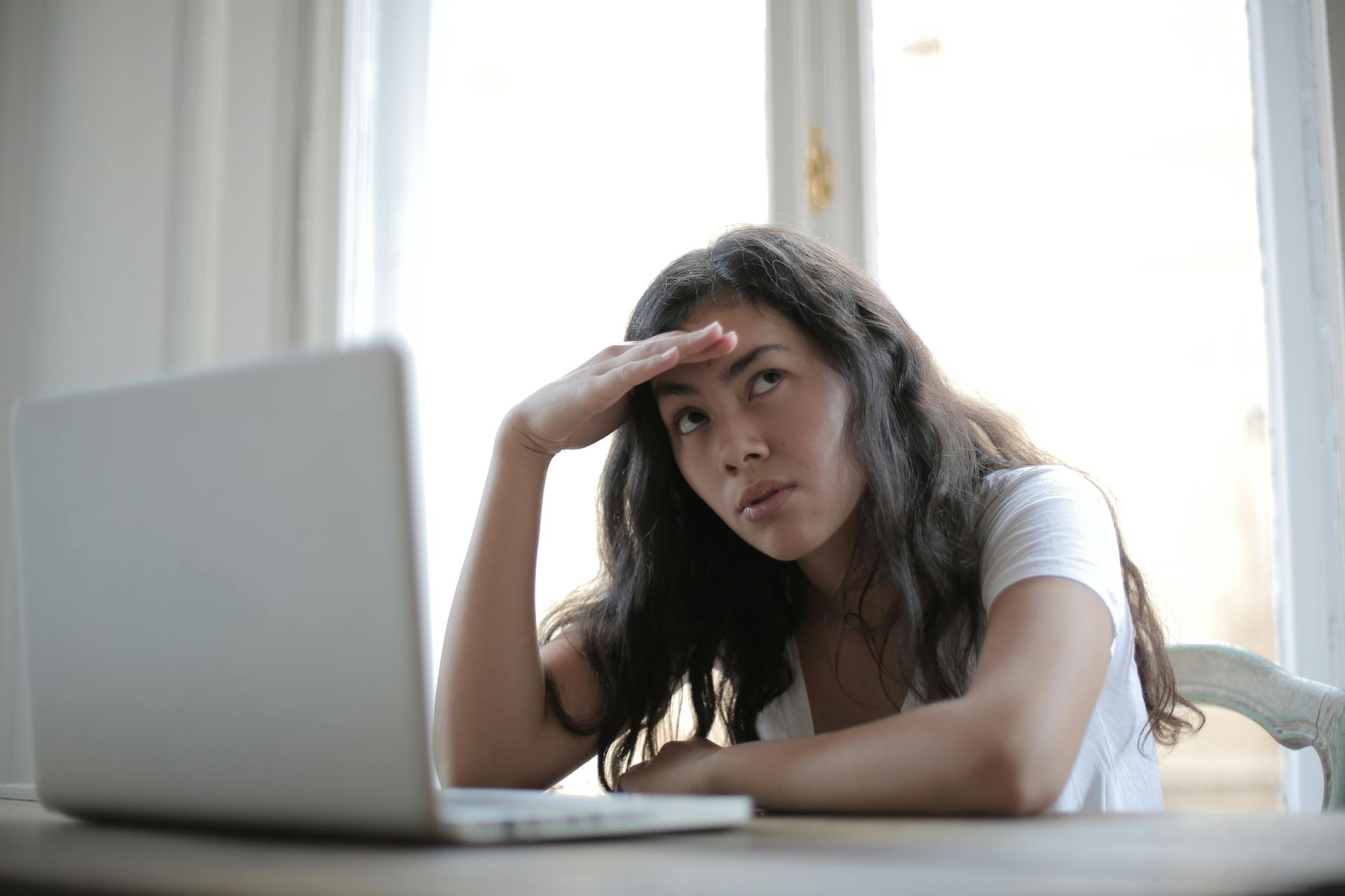woman sitting at desk with laptop head is in her hands