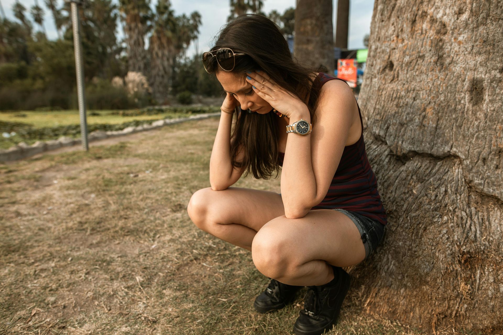 Woman in a park squatting down next to a tree with her head in her hands looked stressed.