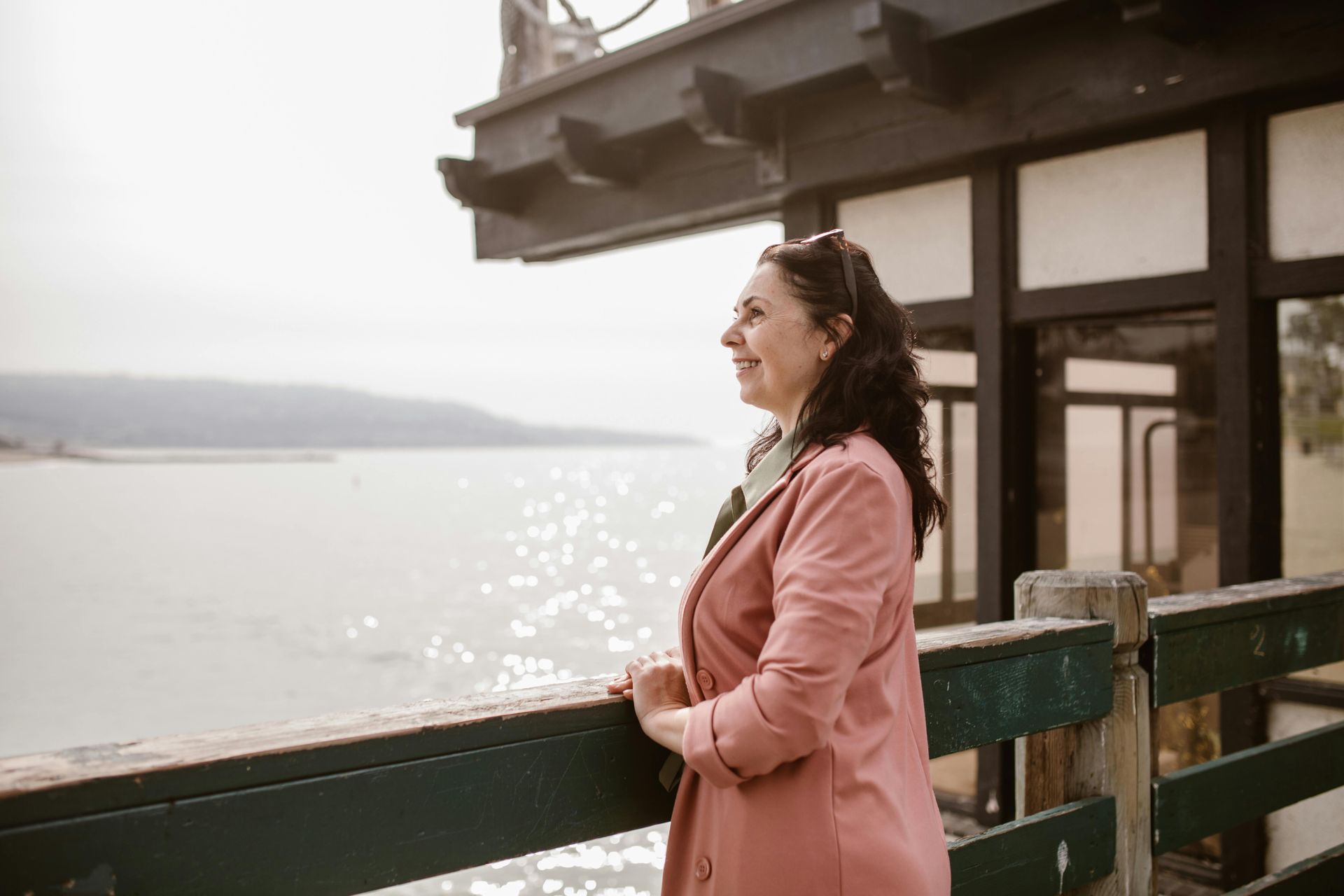 women in a pink jacket leaning on railings looking out to sea
