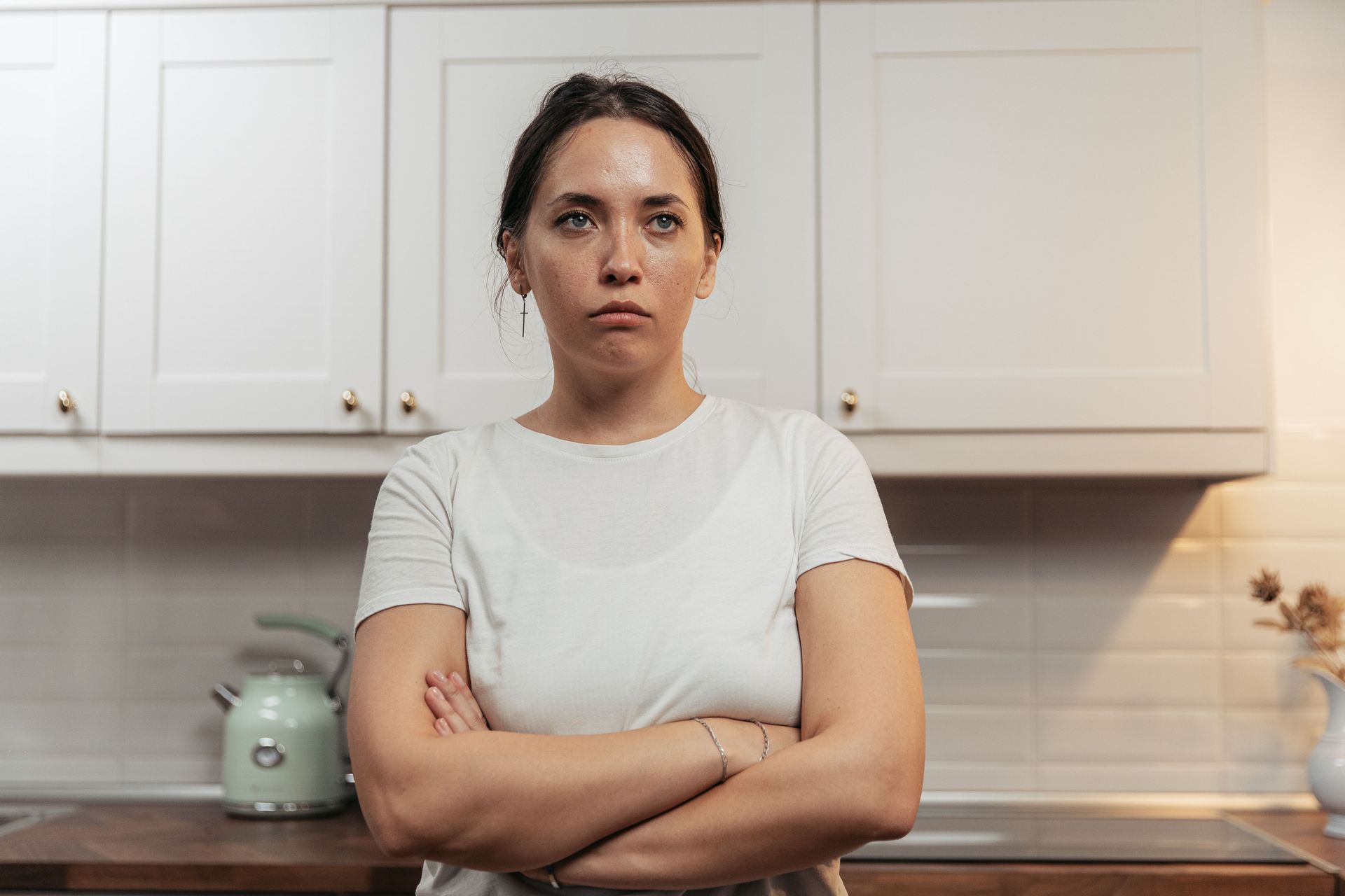 women standing in kitchen with arms crossed looking unhappy