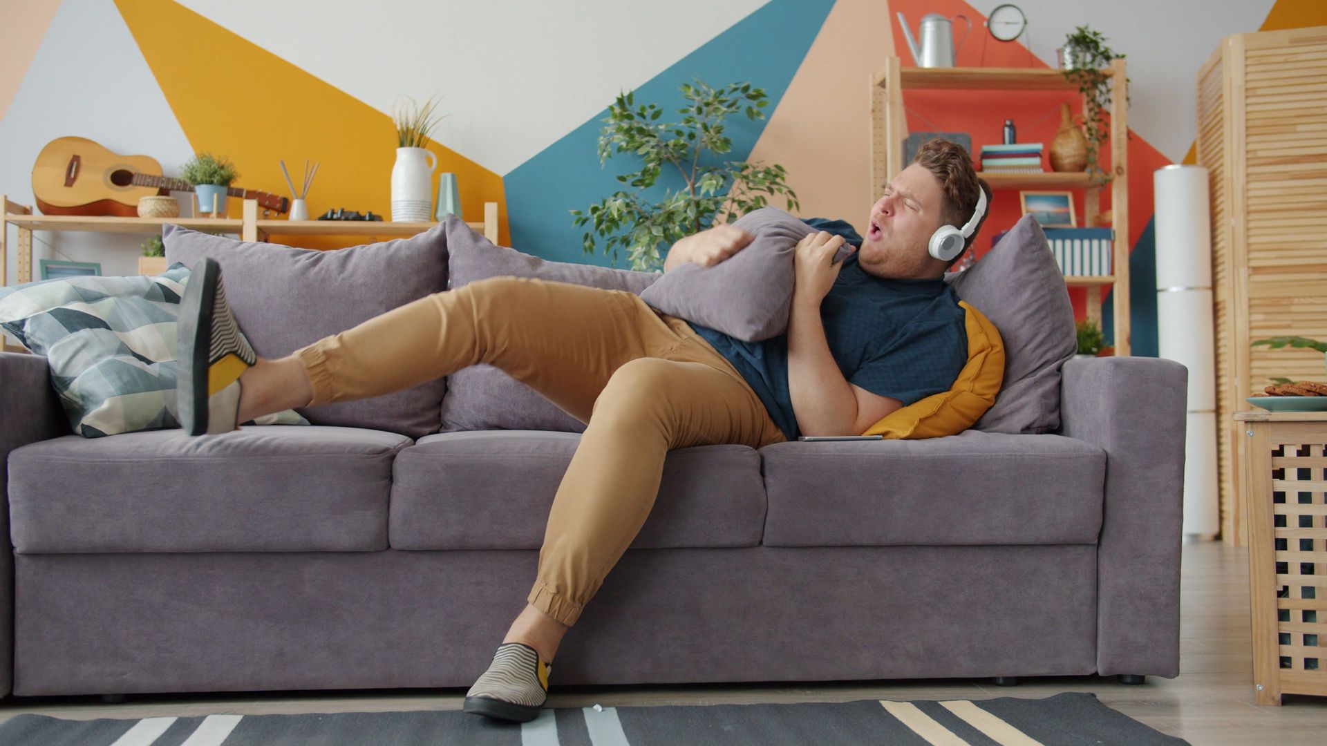man lying on grey sofa looking uncomfortable