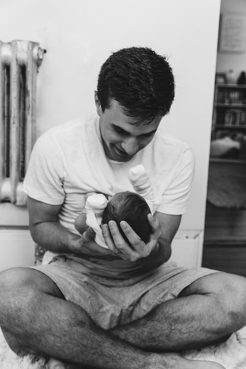 Black and white image of a white father smiling down happily at an infant in his lap.