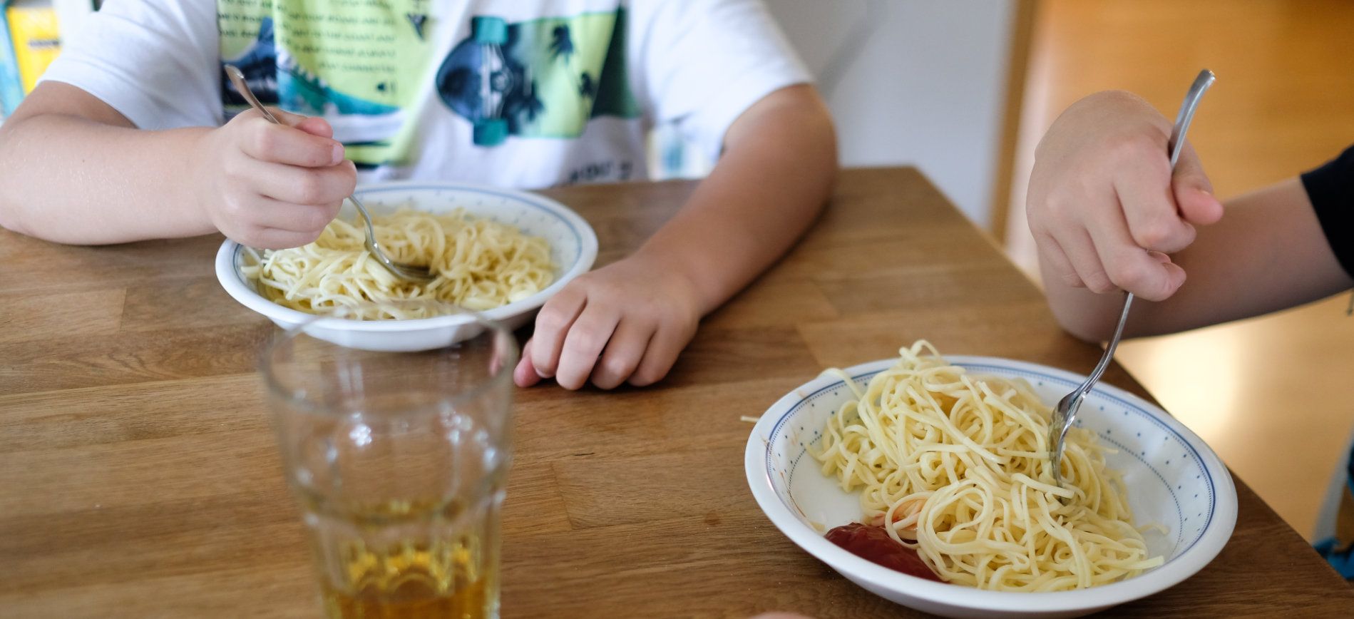 Tischsituation: Kinder essen Nudeln mit einem Klecks Ketchup von einem Teller