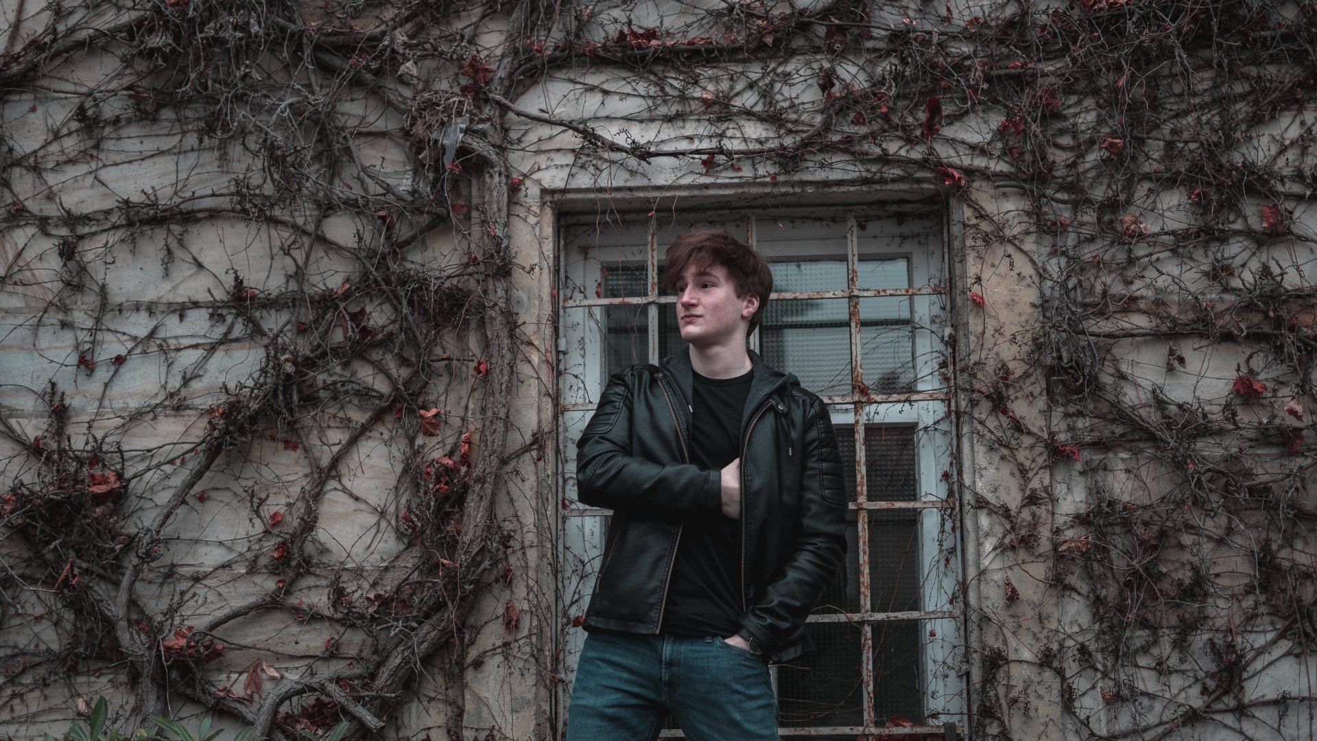 Portrait von jungen Mann in Lederjacke, steht vor altem Fenster und Efeu, Bild von Fotograf Hannes Schmidt