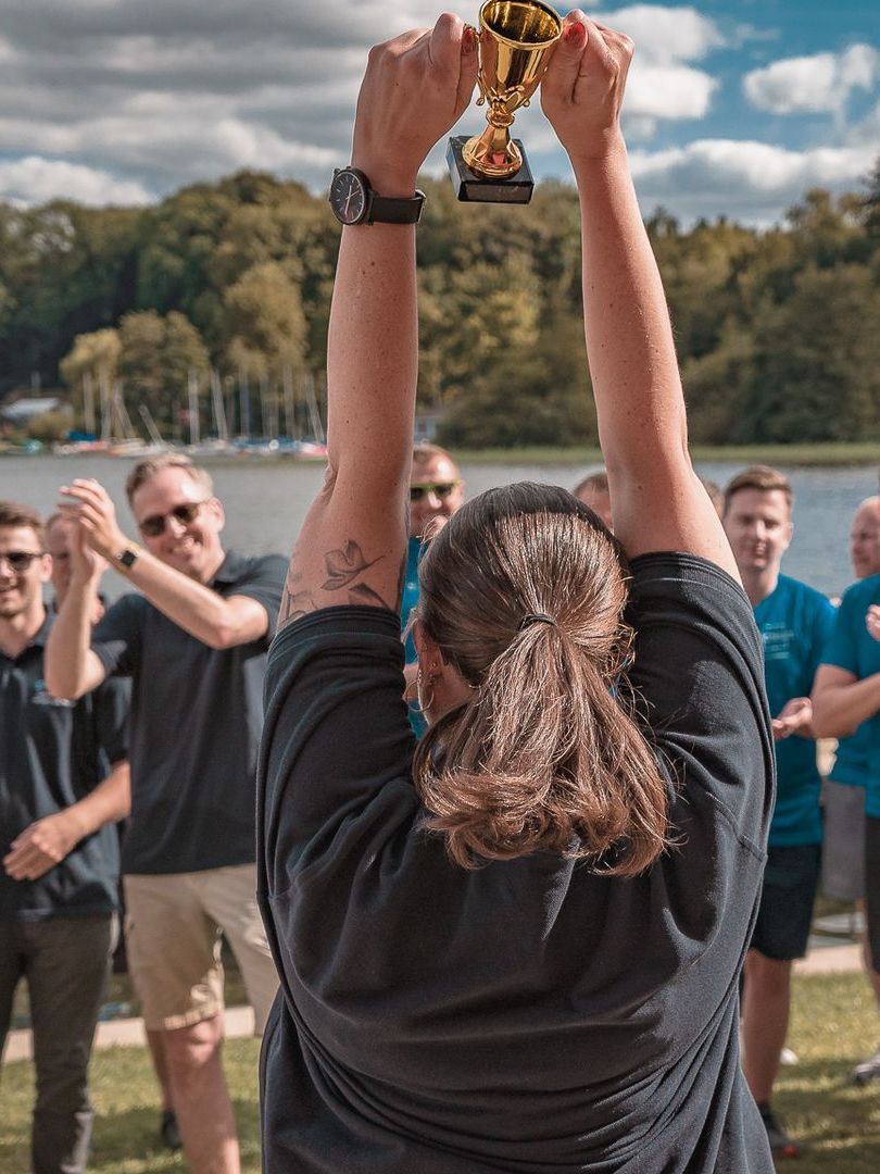 Siegerin hält Trophäe vor ihrem Team hoch