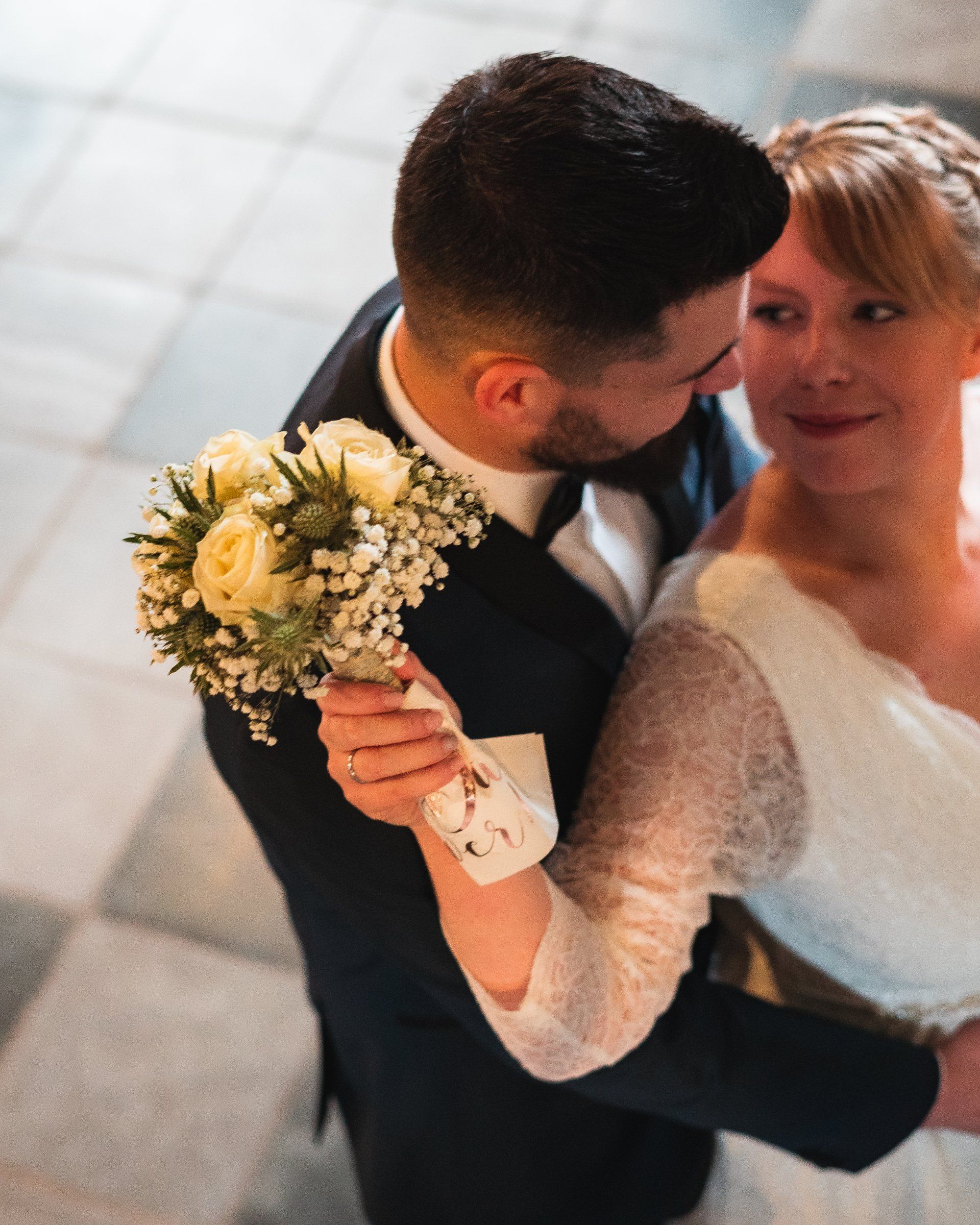 Braut streckt Kranz nach oben, während Bräutigam sie umarmt von Fotograf Hannes Schmidt in Aachen