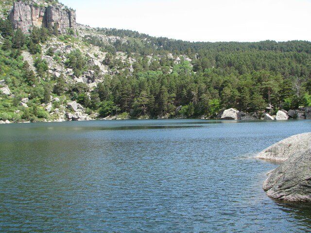 Paisaje glacial de la Laguna Negra de Soria rodeada de pinos y paredes de granito.