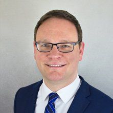 Immobilienmakler Ole Krüger lächelnd mit blauem Sakko, weißem Hemd und Brille