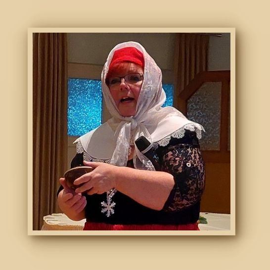 roter langer Rock, schwarze Bluse, breiter weißer Kragen, rote Kappe und darüber ein weißes Spitzenkopftuch, eine Kalimba