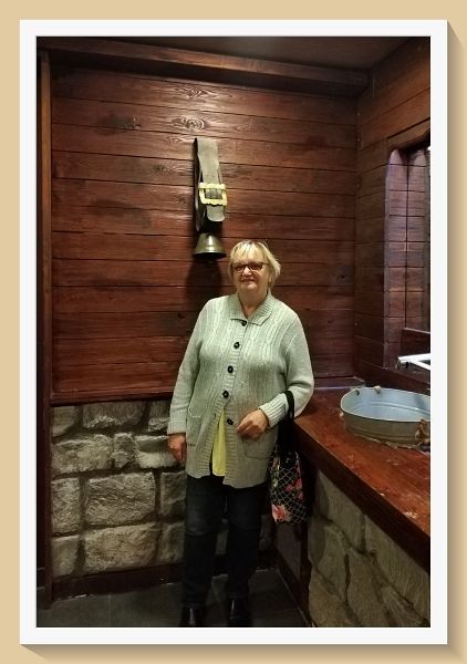 das stille Örtchen, Foto ©Britta Ogasahara Foto: die Toilette gleicht einer Bergstation, Frau steht vor Kuhglocke; Foto ©Britta Ogasahara