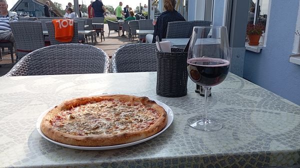 eine große runde Pizza und ein schönes Glas Wein