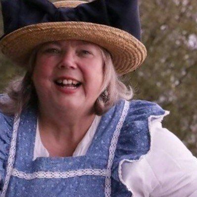 lachendes Portrait von mir, trage eine blaue Schürze mit Rüschen, Strohhut mit großer blauer Schleife,