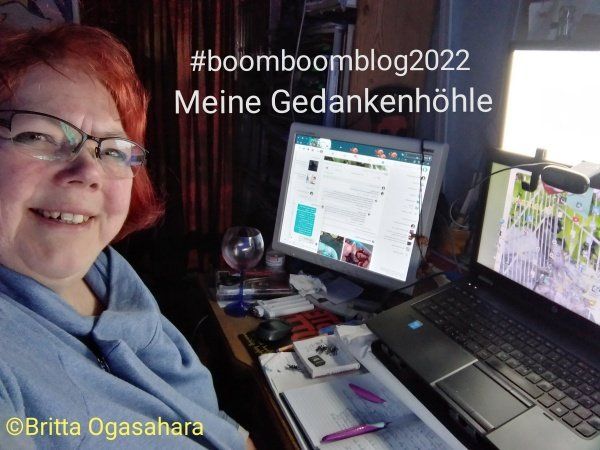 Meine Gedankenhöhle, #boomboomblog2022 Frau sitzt am Schreibtisch und lächelt, darauf ein Laptop und ein 2ter Bildschirm