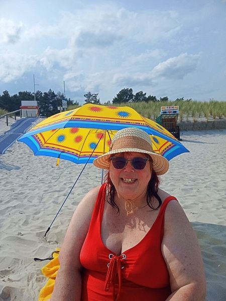 ich sitze mit meinem roten Badeanzug unter einem Sonnenschirm am Strand