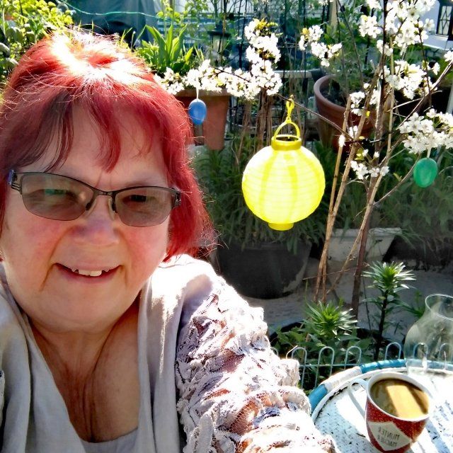 Britta auf dem Balkon, alles blüht Frau mit roten Haaren, im Hintergrund gelbes Lampion, blühender Kirschbaum