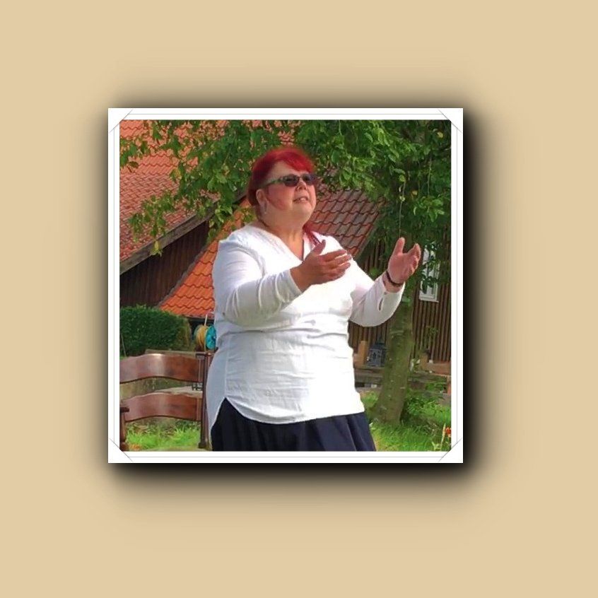 Britta Ogasahara steht mit weit geöffneten Armen und erzählt, Weiße Bluse, langer blauer Rock, Foto ©Gerhild Hustädt