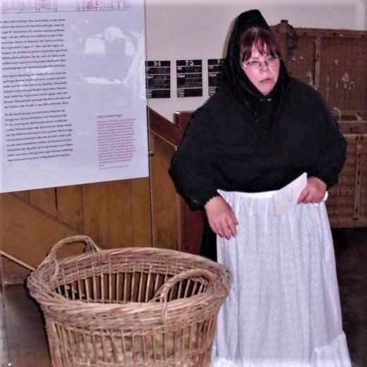 schwarzes Kleid, weiße Schürze, schwarzes Kopftuch (an eine Tracht angelehnt); soll eine Frau aus Böhmen darstellen,