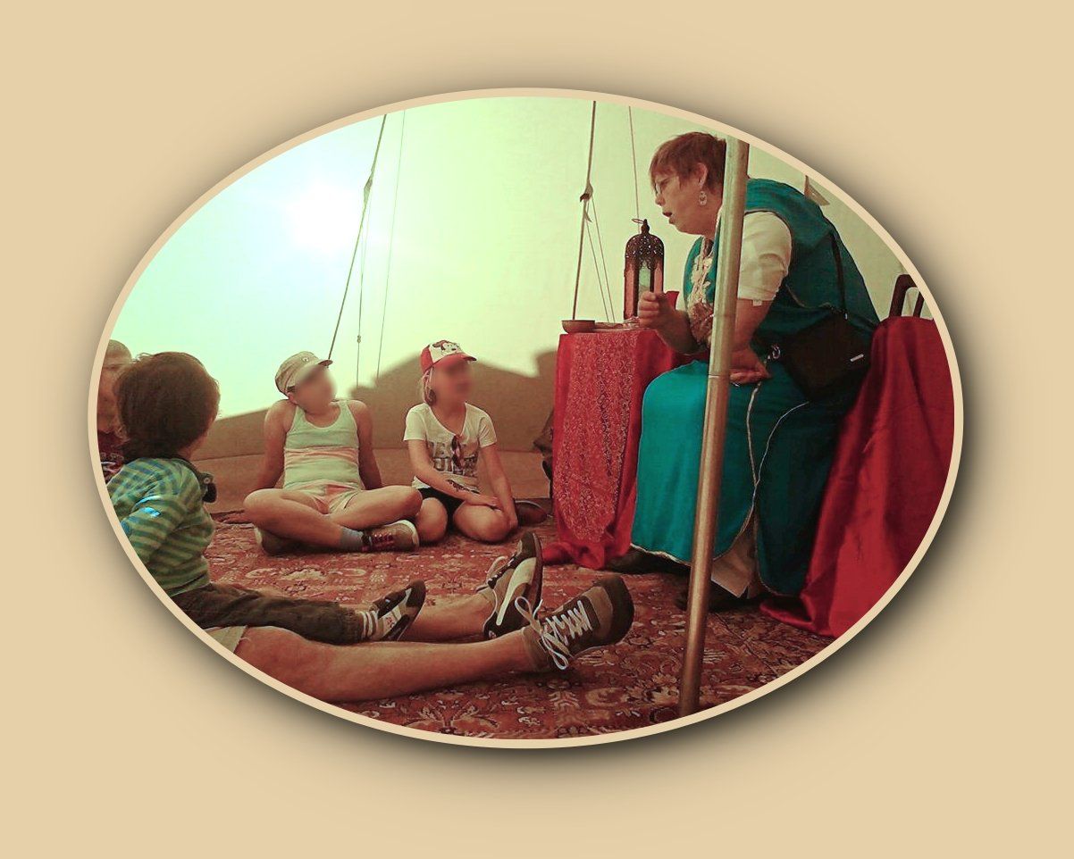 gespannt lauschen die Kinder den Geschichten aus 1000 und 1 Nacht Die Märchenerzählerin Britta Ogasahara in einem blauen langen Kleid, am Boden sitzen 4 Kinder und hören zu