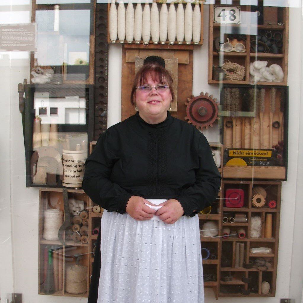 schwarzes Kleid, weiße Schürze, schwarzes Kopftuch (an eine Tracht angelehnt); soll eine Frau aus Böhmen darstellen,