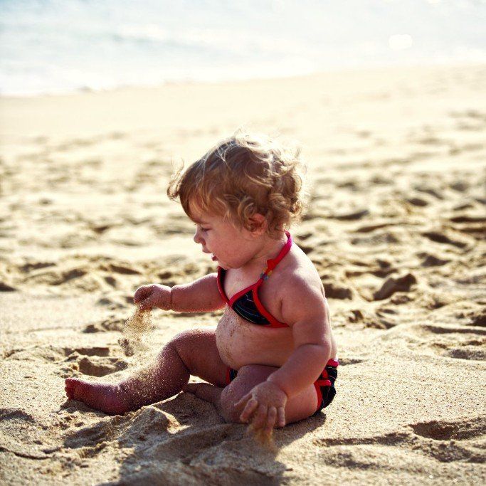 ein kleines Mädchen sitzt am Strand und spielt mit dem Sand