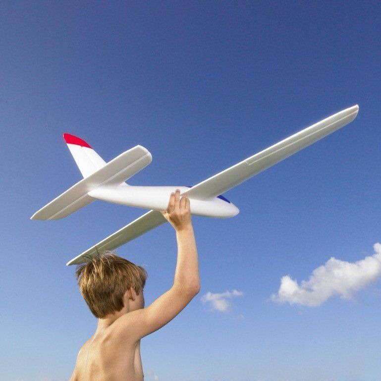 ein Junge wirft mit der rechten Hand einen Modell- Segelflieger in die Luft