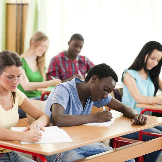 5 Schüler sitzen vor Schultischen in zwei Reihen und schreiben auf ihren Blöcken vor sich