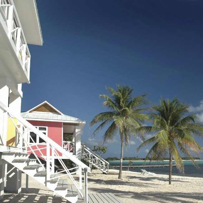 ein rotes und ein gelbes Strand-Haus mit weißen Treppen sind an einem Strand mit Palmen zu sehen