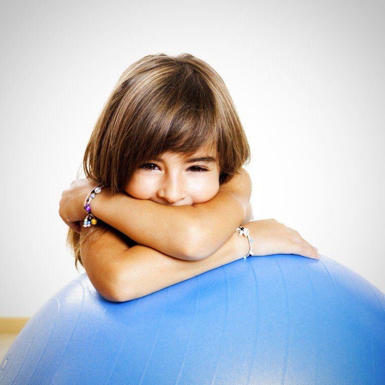 ein Mädchen lehnt sich mit ihren Armen auf einen großen blauen Gummiball und verdeckt dabei ihr Gesicht zur Hälfte mit ihren Armen