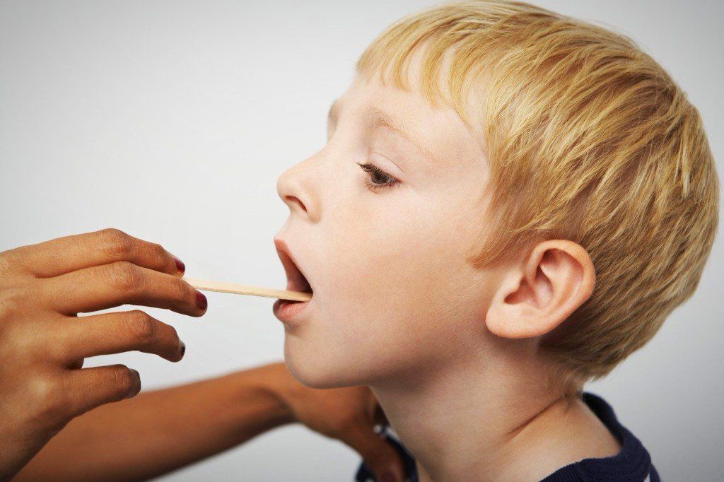 Kopf eines Jungen zu sehen, dessen Mund mit Hilfe eines Holzspatels untersucht wird